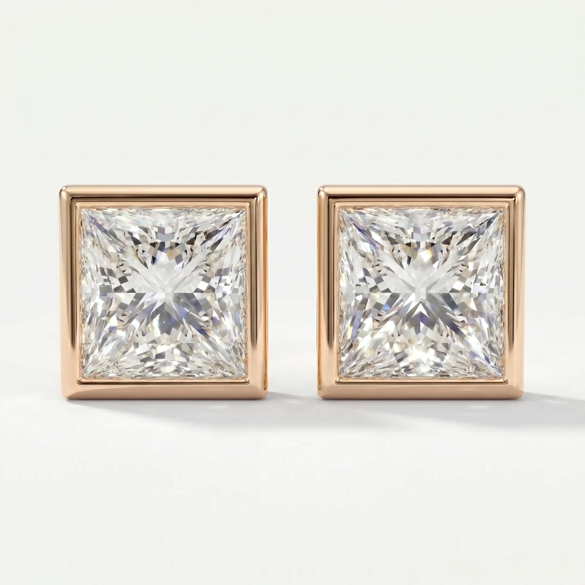 Pair of square-cut diamond earrings with rose gold settings on a white background