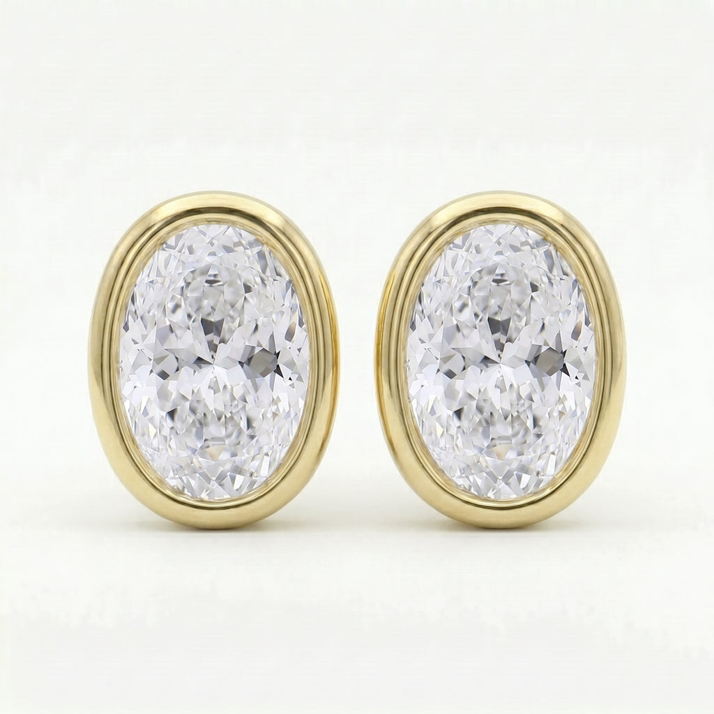Oval bezel-set diamond stud earrings in polished yellow gold with brilliant sparkle on clean white background