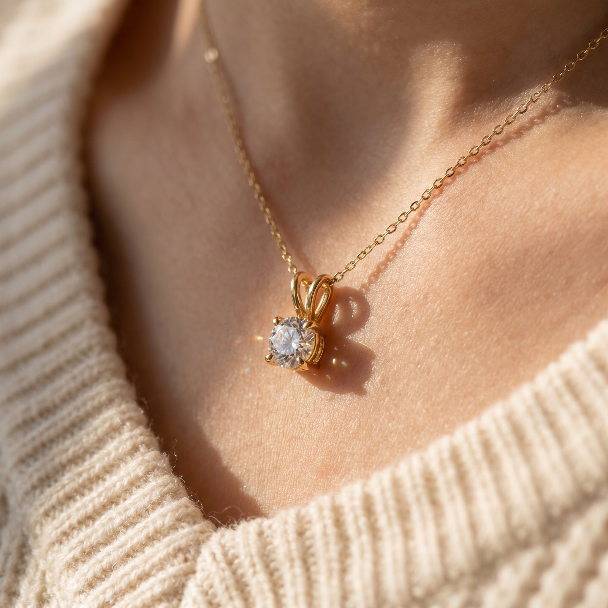 Gold necklace with a diamond pendant on a person wearing a beige sweater.