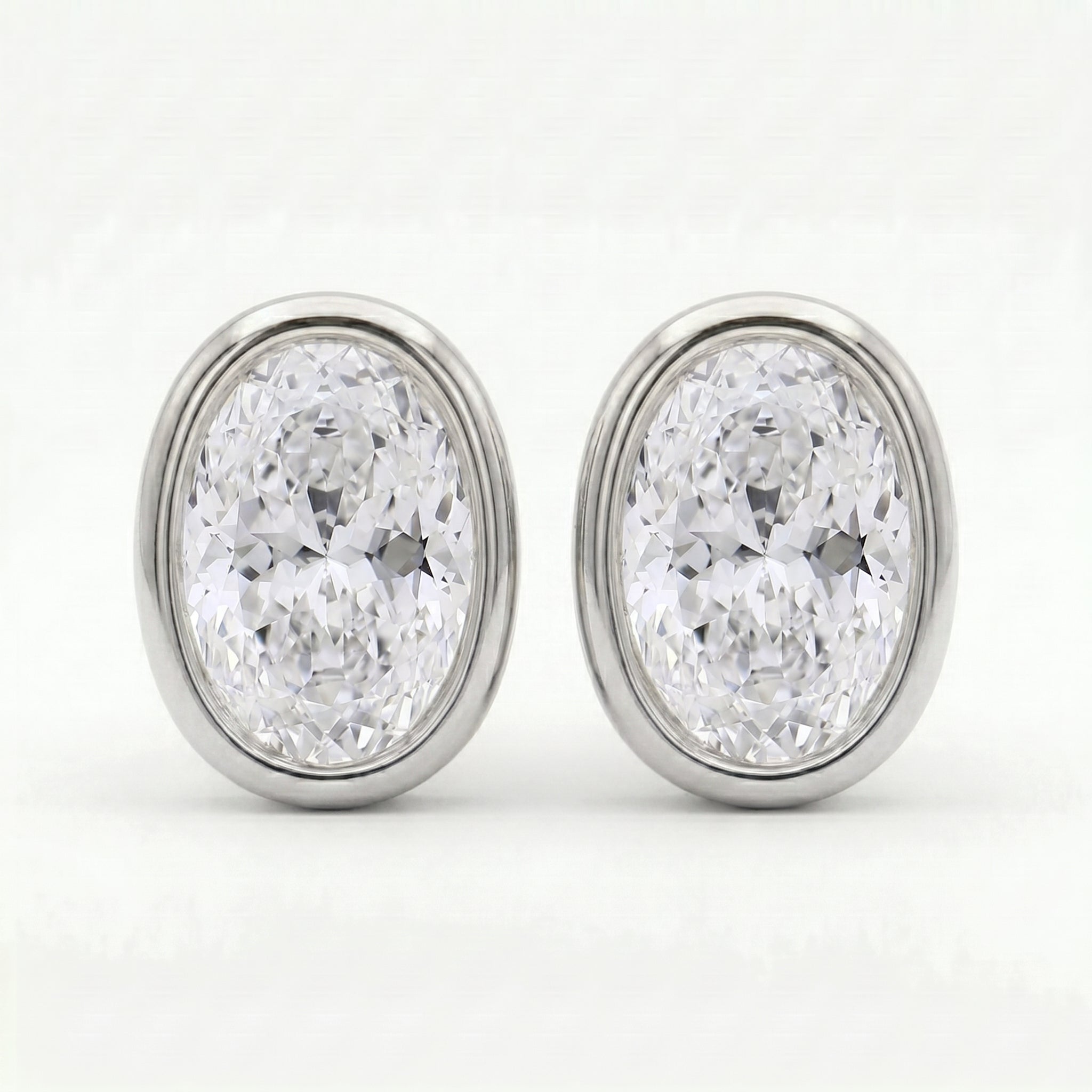Luxury oval diamond bezel earrings angled view highlighting polished gold setting and brilliance