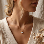Woman wearing a gold necklace with a heart-shaped pendant, holding dried flowers.