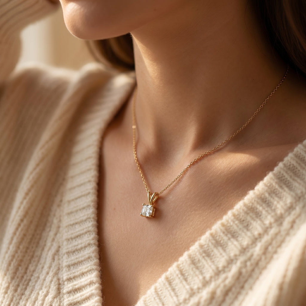 Gold necklace with a diamond pendant worn by a person in a beige sweater.