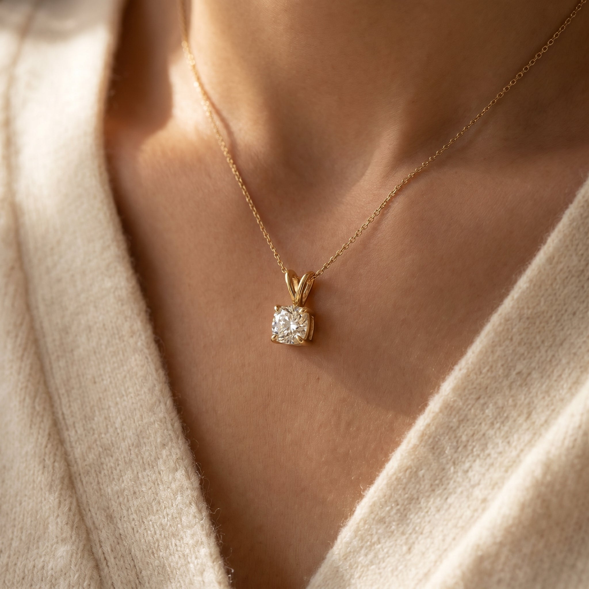 Gold necklace with a diamond pendant worn by a person in a beige sweater.