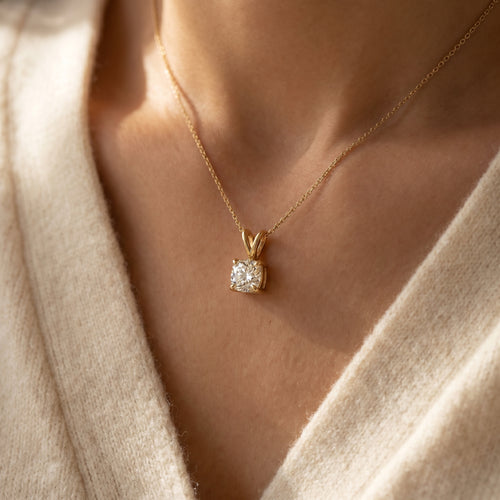 Gold necklace with a diamond pendant worn by a person in a beige sweater.