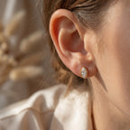 Close-up of a person wearing a gold earring with a blurred natural background