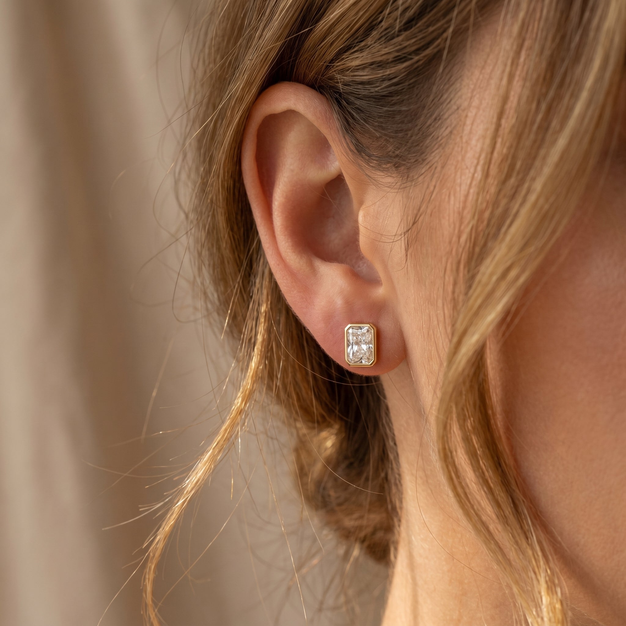 Close-up of an ear wearing a diamond earring with a neutral background