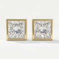 Pair of square-cut diamond earrings with gold prongs on a light gray background