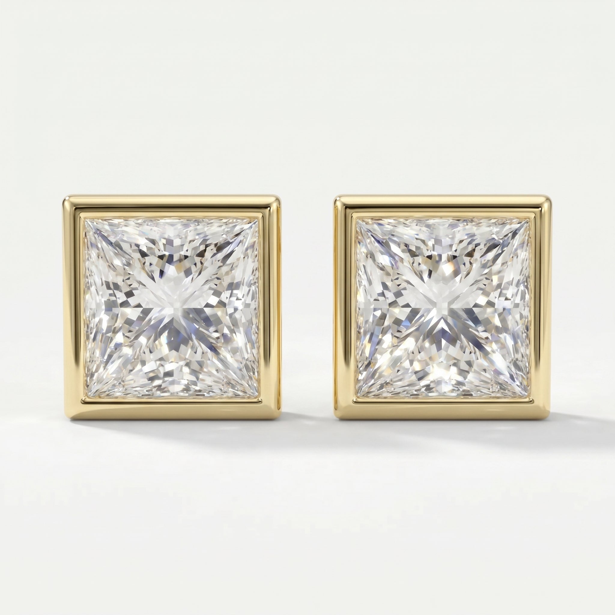 Pair of square-cut diamond earrings with gold prongs on a light gray background