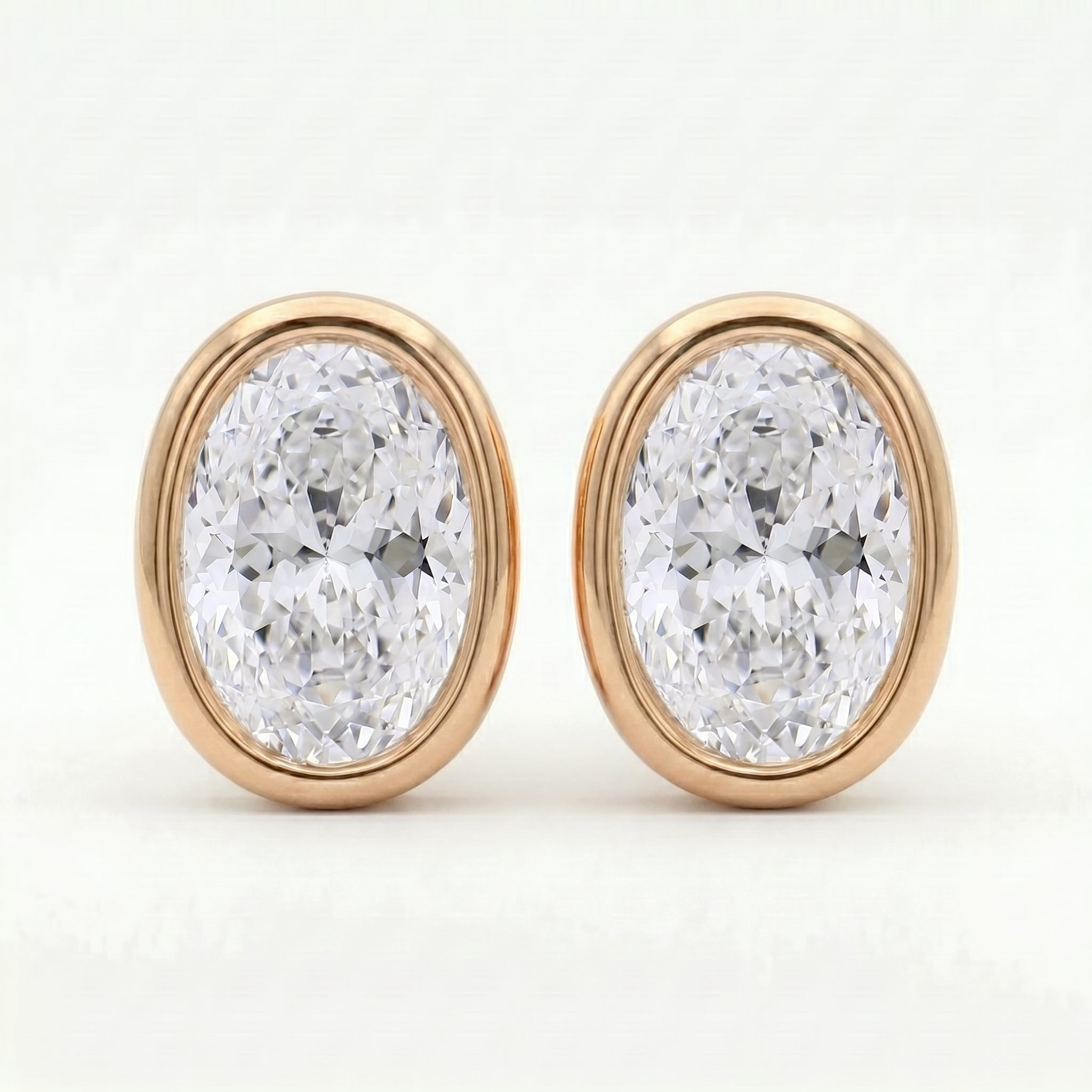 Oval diamond bezel stud earrings in rose gold with brilliant sparkle on clean white background