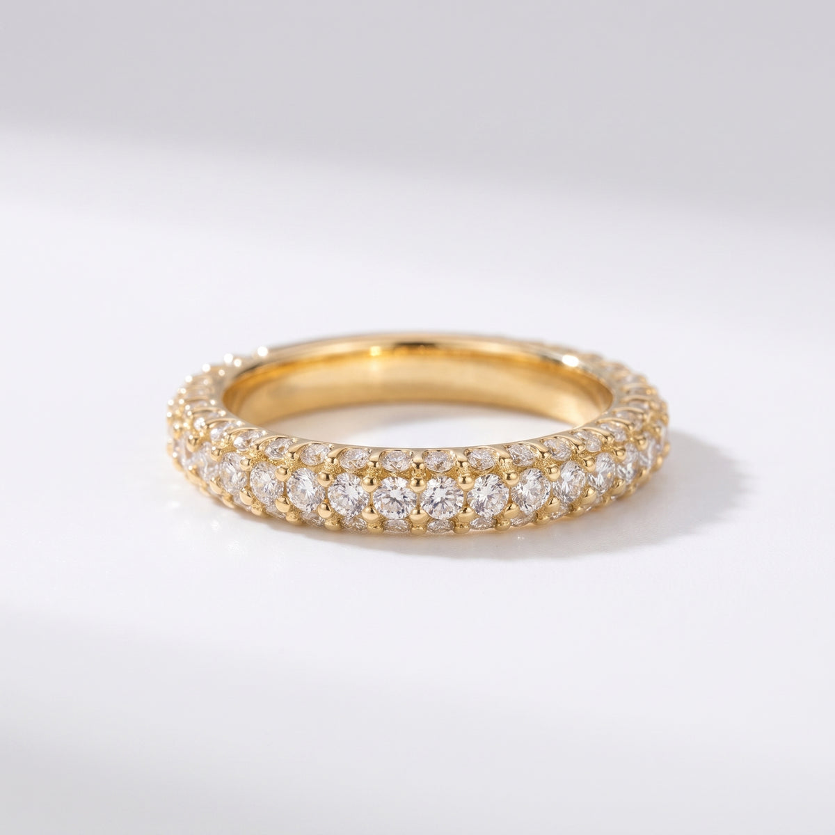 Yellow gold diamond eternity band with three rows of round brilliant pavé diamonds on a pure white background, luxury wedding ring.