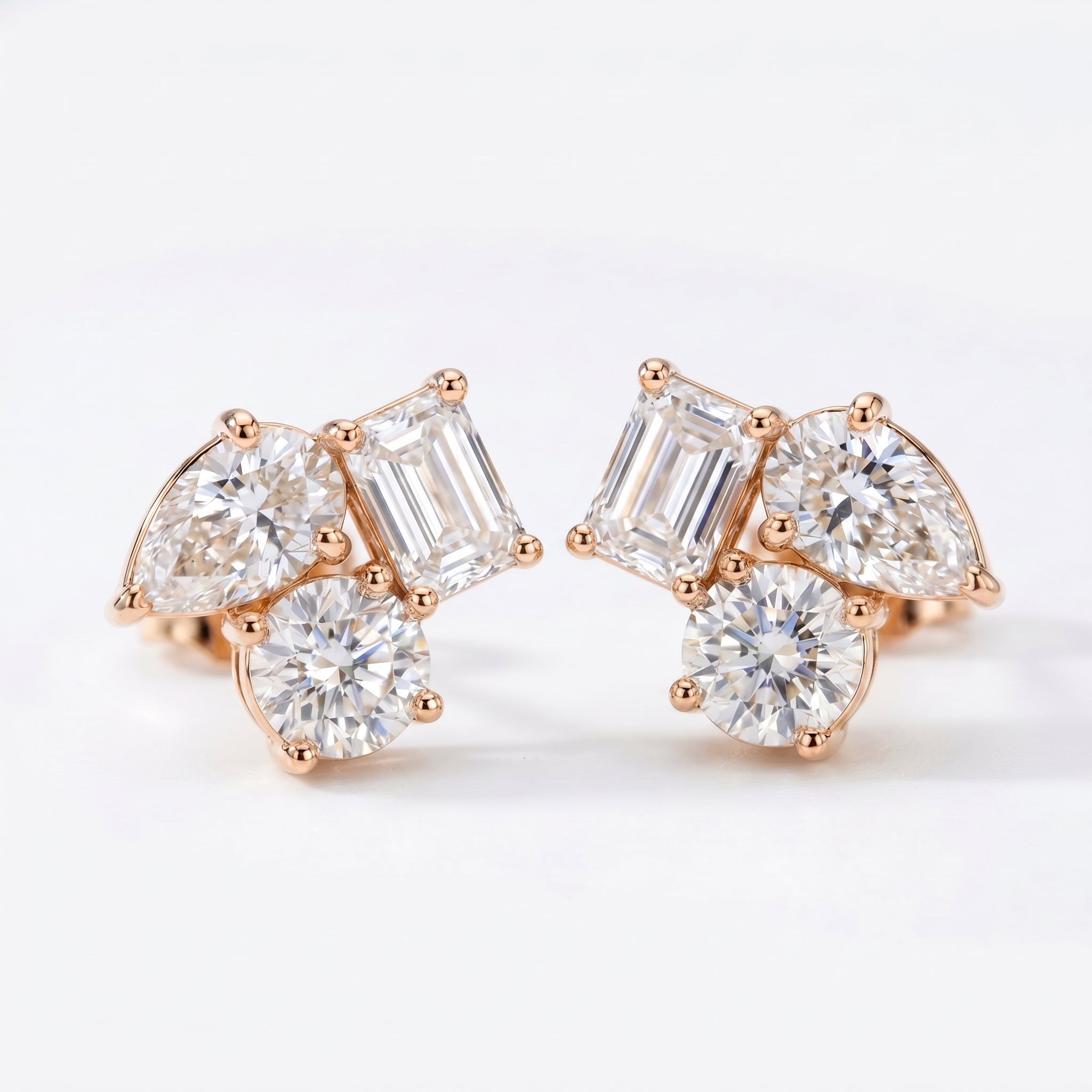 Rose gold diamond cluster stud earrings with pear, emerald and round cut stones on white background