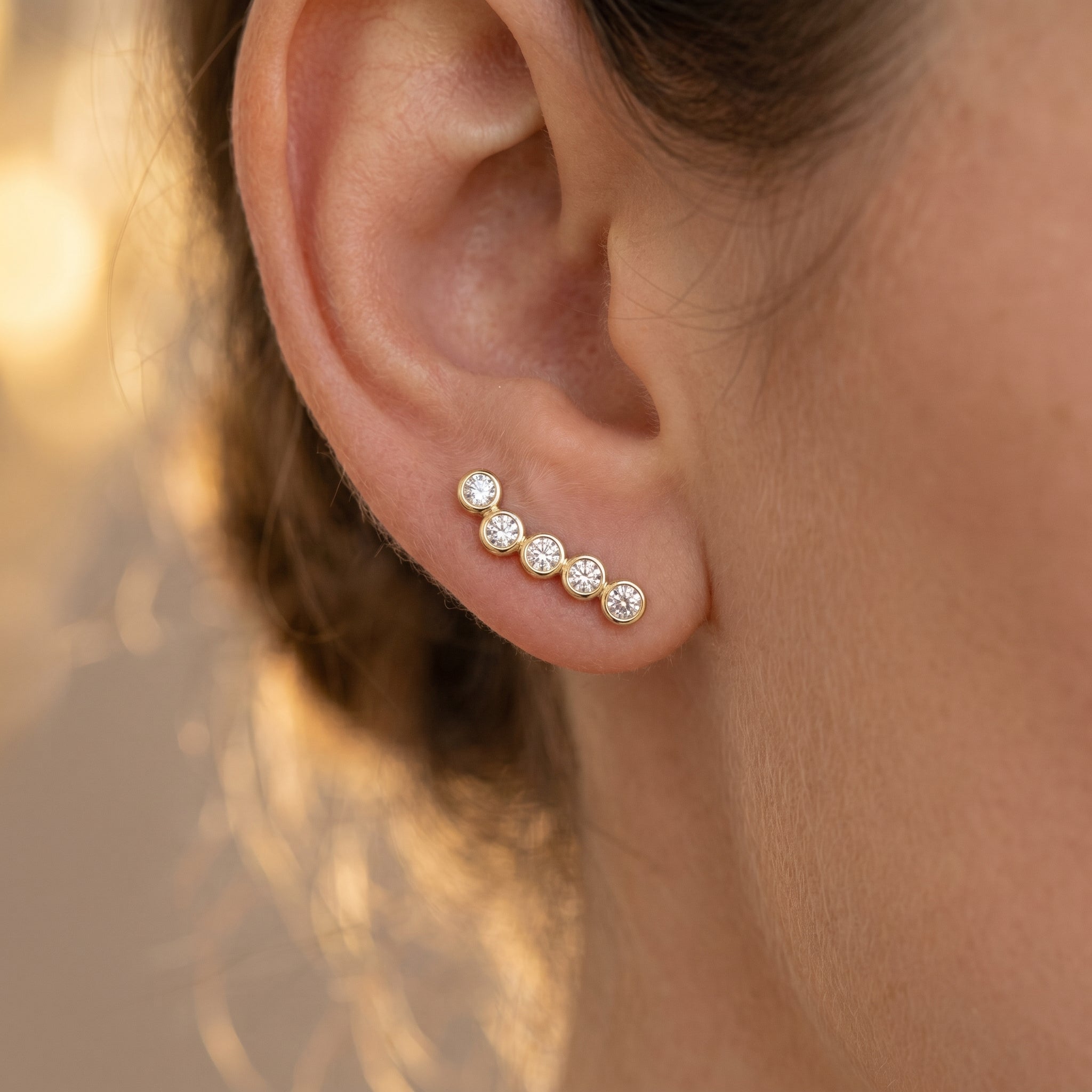 Side profile of bezel-set diamond crawler earrings showing polished gold setting craftsmanship