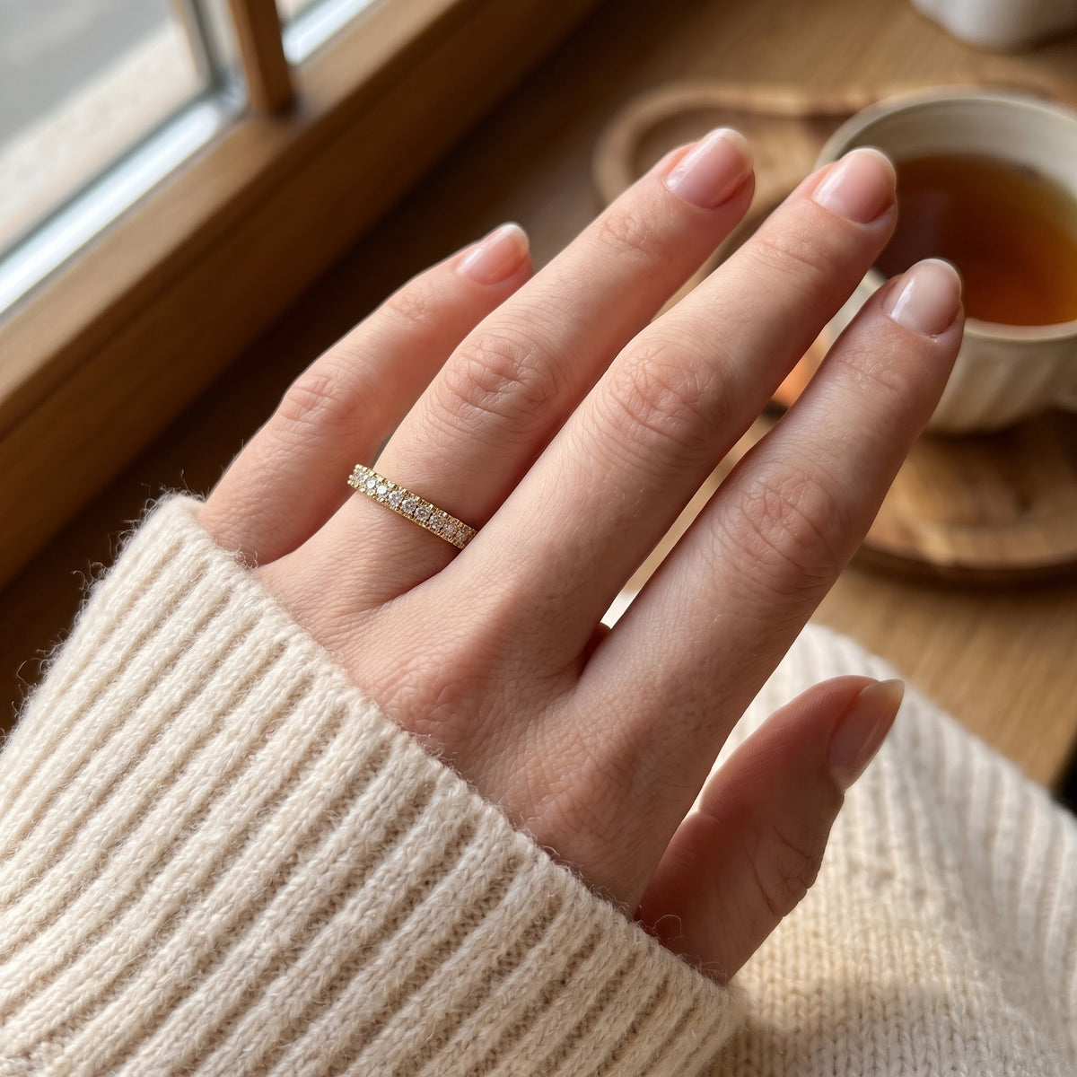 Round diamond eternity ring worn on a woman's finger, showcasing a delicate stackable wedding band in everyday luxury style.