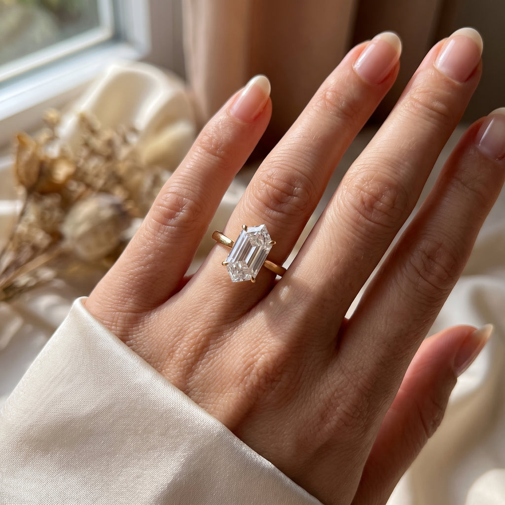 Elongated hexagon solitaire engagement ring worn on hand featuring modern step-cut diamond and slim polished band.